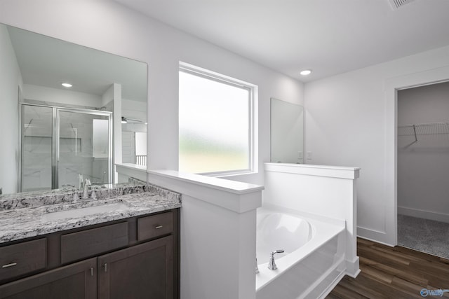 full bathroom with wood finished floors, vanity, a spacious closet, a shower stall, and a bath