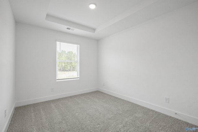 empty room featuring a tray ceiling, carpet, visible vents, and baseboards