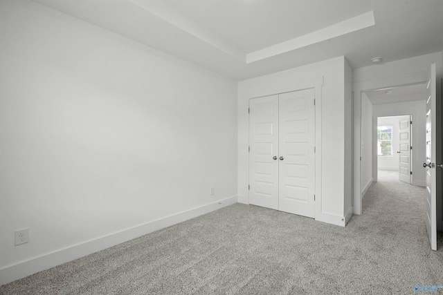 unfurnished bedroom with a tray ceiling, light colored carpet, and baseboards