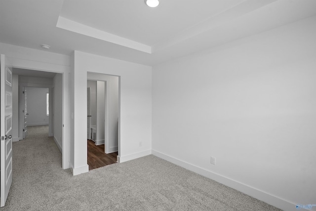 unfurnished bedroom with baseboards, dark carpet, and a raised ceiling