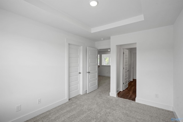 unfurnished bedroom featuring a tray ceiling, baseboards, and dark colored carpet