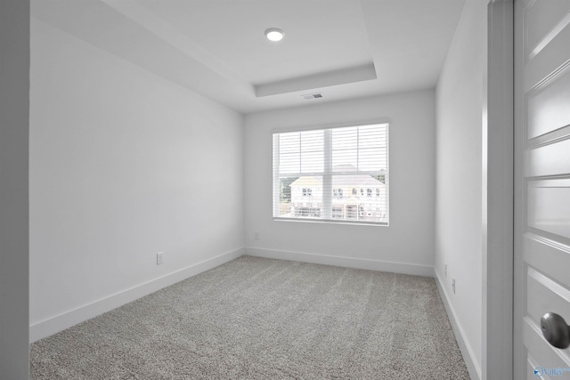 carpeted empty room featuring a tray ceiling, visible vents, and baseboards