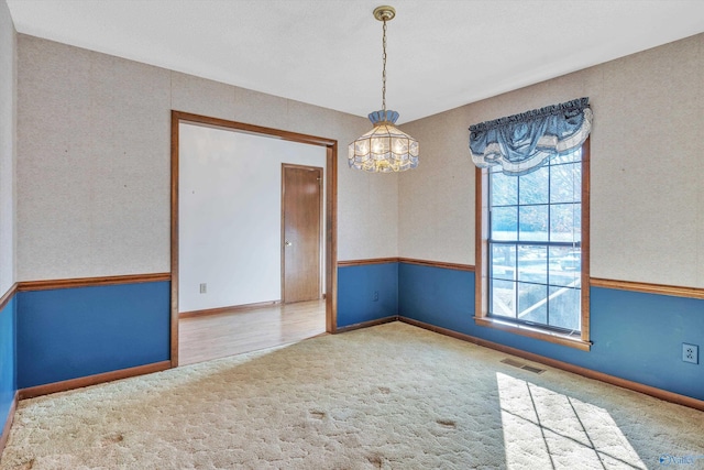 carpeted empty room featuring an inviting chandelier