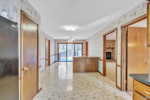 kitchen with ceiling fan, a textured ceiling, and a stone fireplace