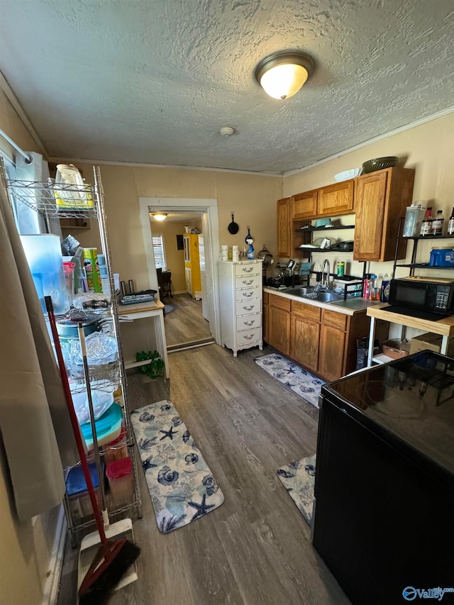 kitchen with dark wood-type flooring, black appliances, sink, ornamental molding, and a textured ceiling