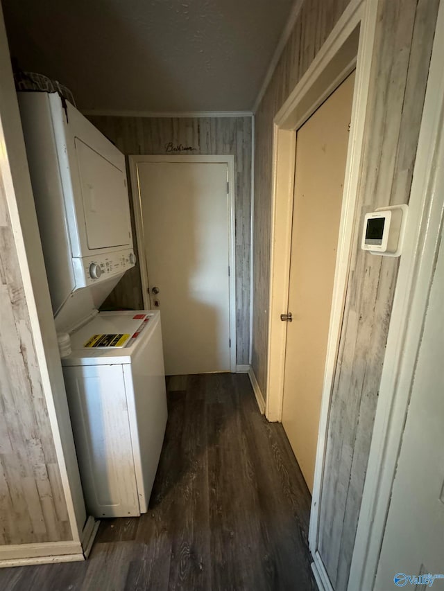 laundry room with stacked washer and dryer, crown molding, dark hardwood / wood-style floors, and wooden walls