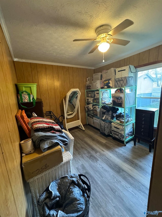 bedroom with ceiling fan, crown molding, wood-type flooring, and wood walls