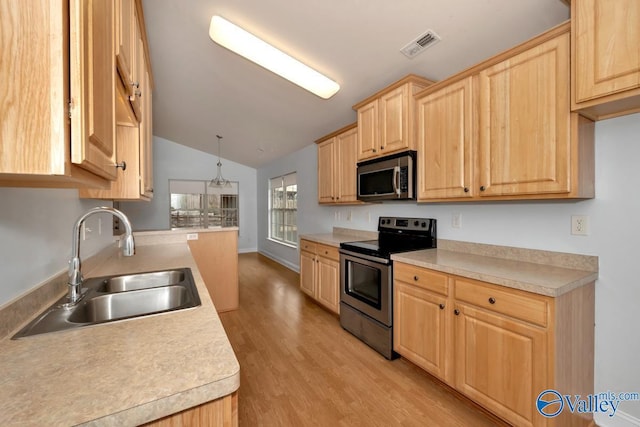 kitchen featuring light brown cabinetry, lofted ceiling, sink, hanging light fixtures, and stainless steel appliances