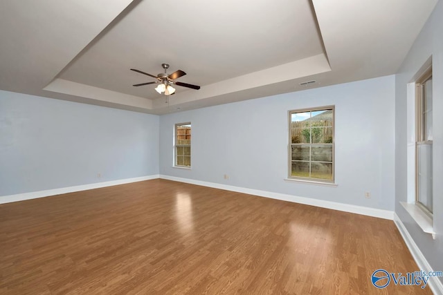 empty room featuring a raised ceiling, ceiling fan, and light hardwood / wood-style flooring