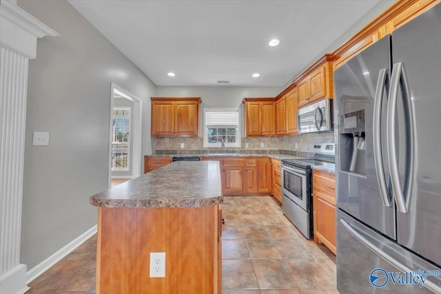 kitchen with tasteful backsplash, baseboards, a kitchen island, appliances with stainless steel finishes, and a sink