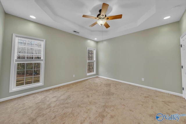 empty room with a tray ceiling, visible vents, and baseboards