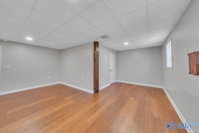 basement featuring a paneled ceiling, visible vents, baseboards, and wood finished floors