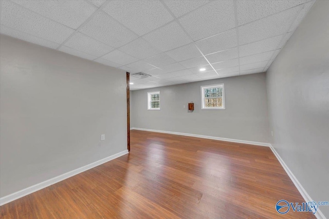 below grade area featuring a paneled ceiling, baseboards, and wood finished floors