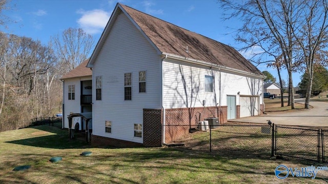 view of side of home with driveway, a lawn, an attached garage, fence, and brick siding