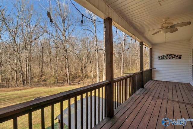 deck with ceiling fan, a forest view, and a lawn