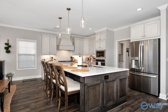 kitchen with custom range hood, appliances with stainless steel finishes, light countertops, crown molding, and a sink