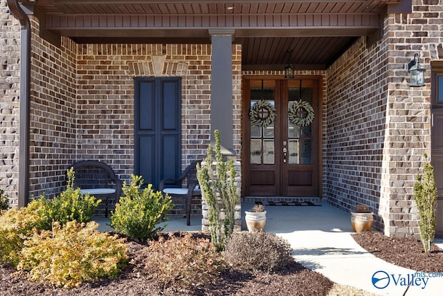 view of exterior entry featuring french doors, a porch, and brick siding