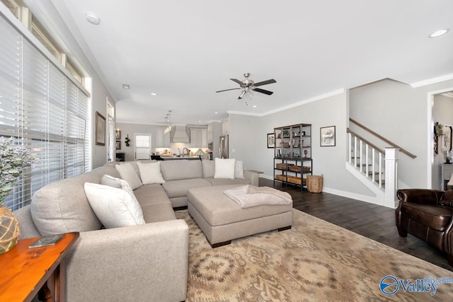 living area featuring dark wood-style floors, crown molding, a ceiling fan, baseboards, and stairs