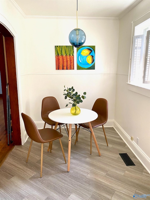 dining space with ornamental molding and light hardwood / wood-style flooring