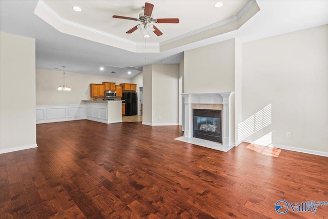 unfurnished living room featuring a premium fireplace, dark wood finished floors, crown molding, a raised ceiling, and ceiling fan with notable chandelier