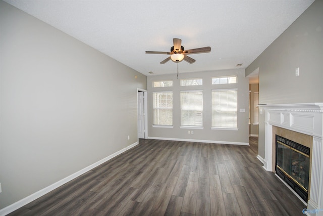 unfurnished living room with a tile fireplace, dark wood finished floors, baseboards, and ceiling fan