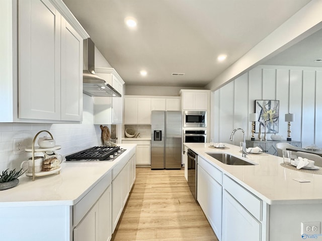 kitchen with wall chimney range hood, white cabinets, stainless steel appliances, and sink