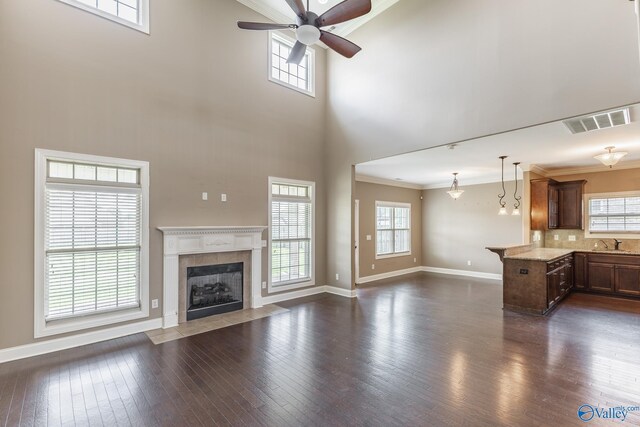 unfurnished living room with sink, a tile fireplace, ceiling fan, and dark wood-type flooring