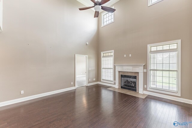 unfurnished living room featuring wood-type flooring, ceiling fan, a towering ceiling, and a tiled fireplace