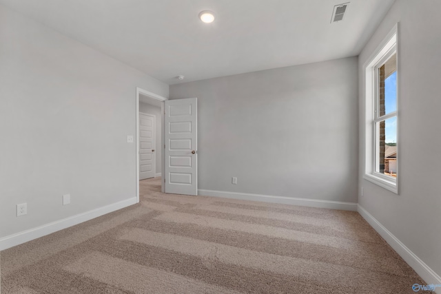 unfurnished bedroom featuring multiple windows, light colored carpet, and ensuite bath