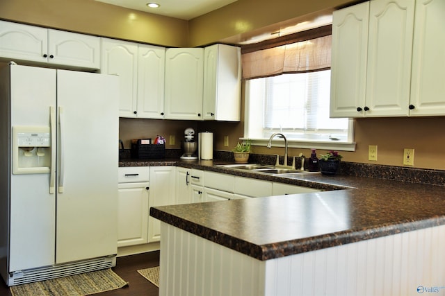 kitchen with white refrigerator with ice dispenser, white cabinets, kitchen peninsula, and sink