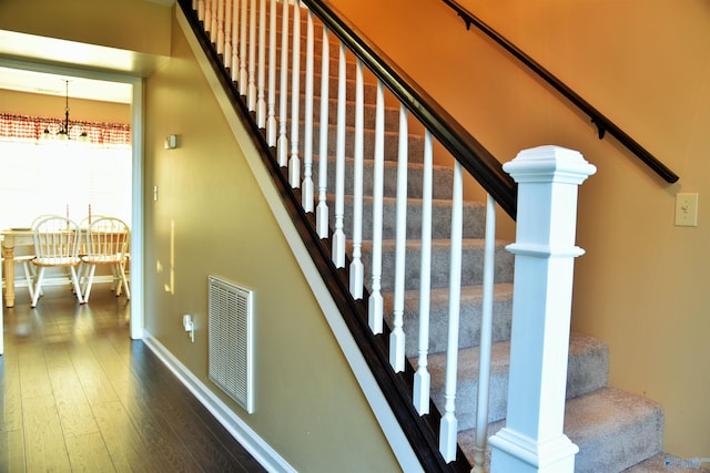 stairs with hardwood / wood-style floors and a notable chandelier