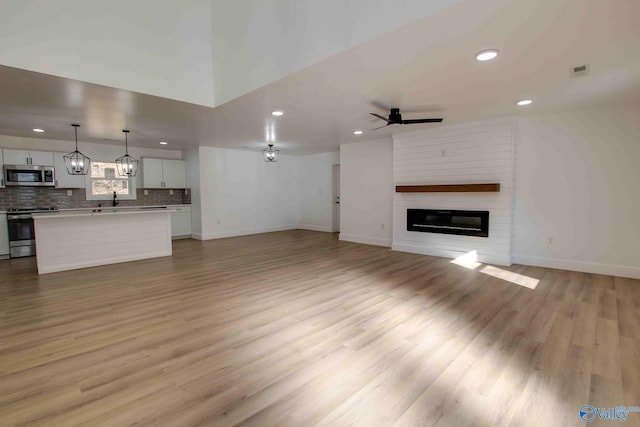 unfurnished living room featuring ceiling fan, light wood-type flooring, and sink