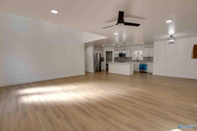 unfurnished living room featuring ceiling fan, sink, and light wood-type flooring