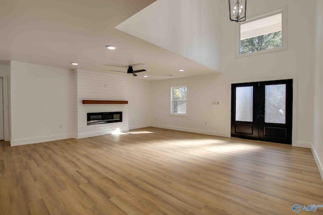 unfurnished living room featuring a large fireplace, ceiling fan, light hardwood / wood-style flooring, and french doors