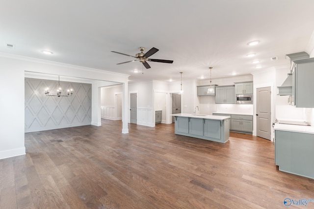 kitchen featuring pendant lighting, ceiling fan with notable chandelier, stainless steel microwave, and an island with sink