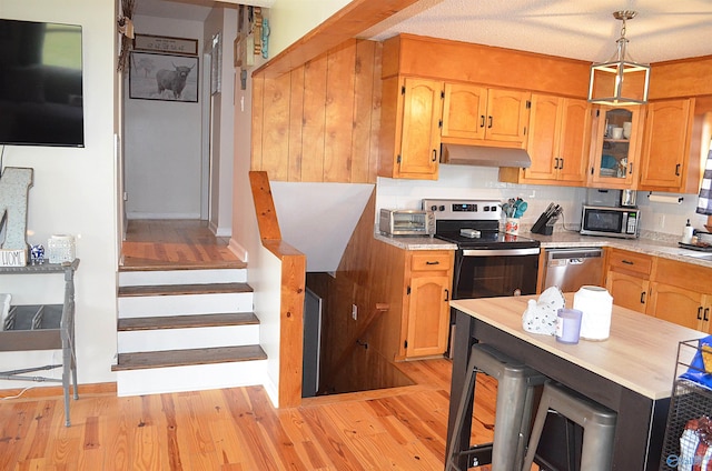 kitchen with appliances with stainless steel finishes, light wood-type flooring, tasteful backsplash, a textured ceiling, and hanging light fixtures