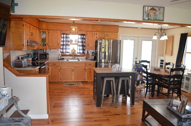 kitchen with pendant lighting, sink, light wood-type flooring, range hood, and appliances with stainless steel finishes