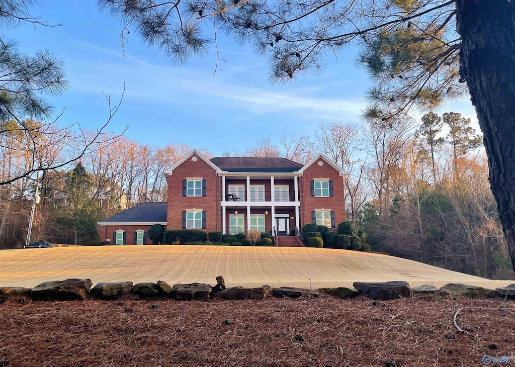 view of front facade featuring brick siding, a front lawn, and a balcony