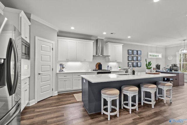 kitchen featuring a kitchen island with sink, white cabinetry, stainless steel appliances, and wall chimney range hood