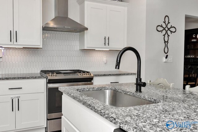 kitchen featuring a sink, white cabinetry, wall chimney exhaust hood, tasteful backsplash, and gas range