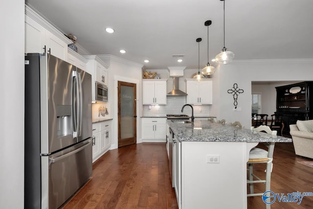 kitchen with a center island with sink, wall chimney exhaust hood, appliances with stainless steel finishes, light stone counters, and white cabinetry