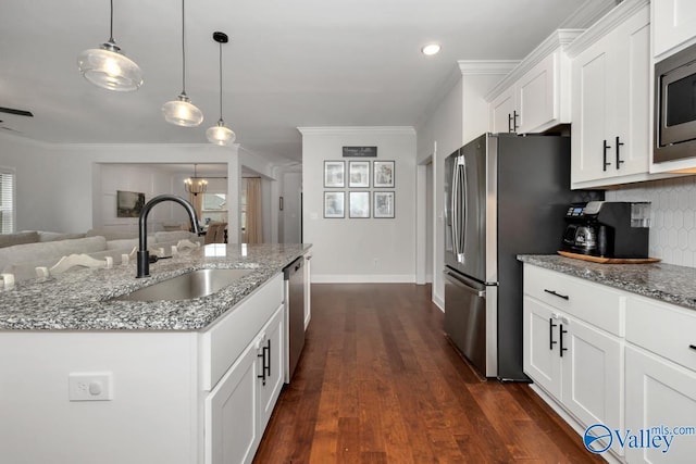 kitchen featuring hanging light fixtures, appliances with stainless steel finishes, white cabinets, a sink, and light stone countertops