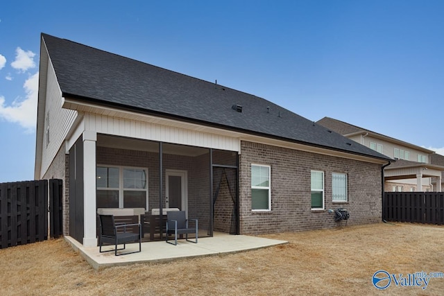 rear view of property with a shingled roof, brick siding, fence, and a patio