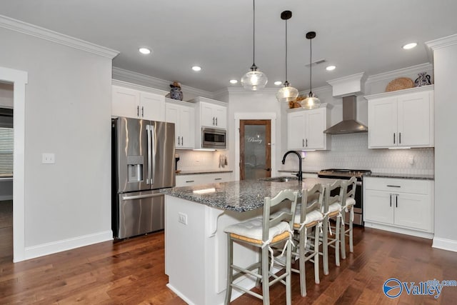 kitchen featuring stainless steel appliances, white cabinets, a kitchen island with sink, a sink, and wall chimney exhaust hood