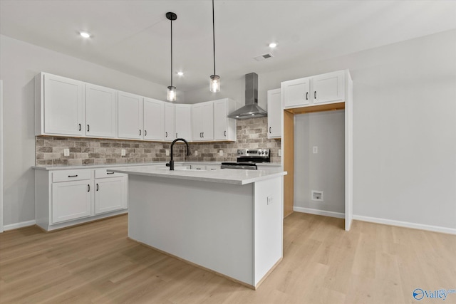 kitchen with white cabinetry, wall chimney range hood, a center island with sink, and stainless steel stove