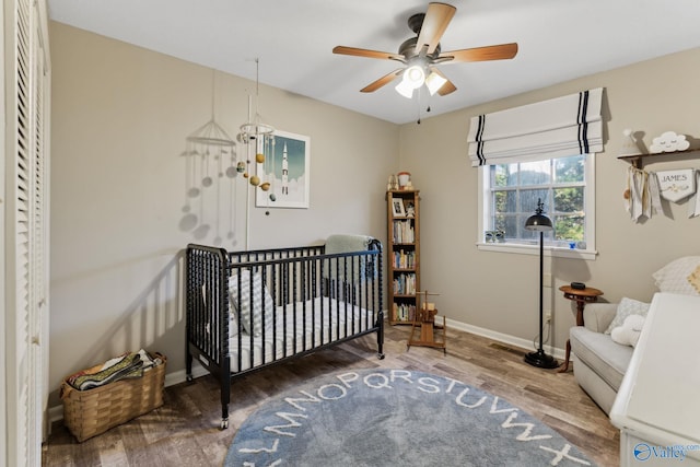 bedroom with ceiling fan with notable chandelier, wood-type flooring, and a crib