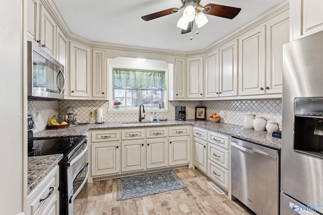 kitchen featuring appliances with stainless steel finishes, tasteful backsplash, light stone counters, sink, and light hardwood / wood-style floors