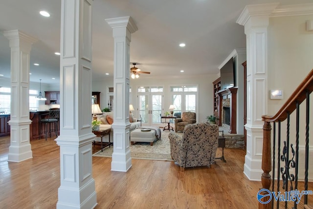 living room featuring ornamental molding, ceiling fan, a stone fireplace, and light hardwood / wood-style floors