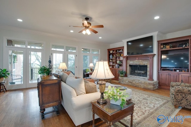 living room with french doors, a fireplace, ceiling fan, crown molding, and light wood-type flooring