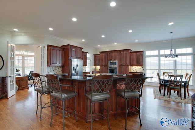 kitchen featuring ornamental molding, light wood-type flooring, appliances with stainless steel finishes, a large island, and a kitchen bar